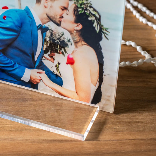 Close-up acrylic desk print of a bride and groom kissing, highlighting the clear acrylic edge and modern stand on a wooden surface.