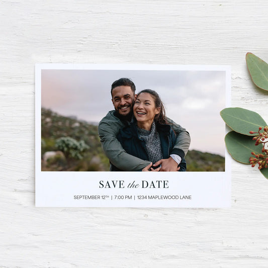 Flat save-the-date card with landscape engagement photo and serif typography on white background with eucalyptus leaves.