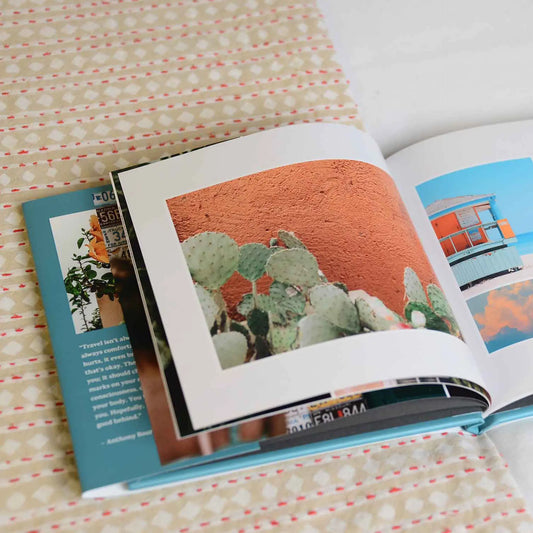 Open hardcover photo book displaying a travel-themed interior spread with a cactus photograph and additional images on adjacent pages