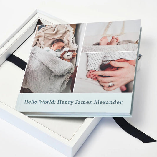 Layflat photo book resting in a white keepsake box, displaying newborn details including tiny feet and hands on a clean, minimal background