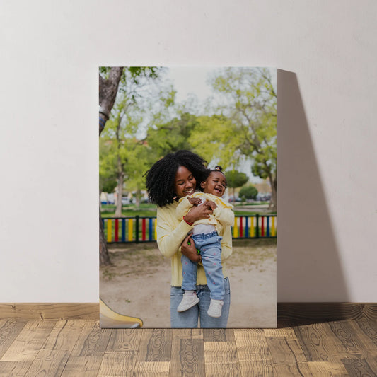 Mounted photo print featuring a woman holding a young child at a playground, leaning against a wall on a light wood floor.