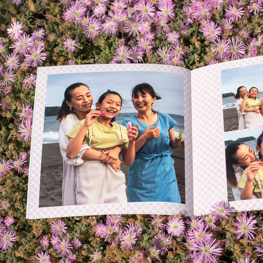 Softcover photo book opened on a floral background, featuring a family group smiling at the beach with ocean waves visible behind them