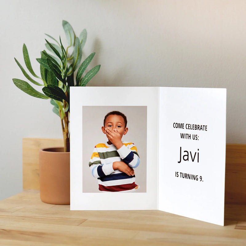 Folded birthday invitation card displayed open on a table, showing a child’s portrait on the left and text on the right reading “Come celebrate with us: Javi is turning 9.”