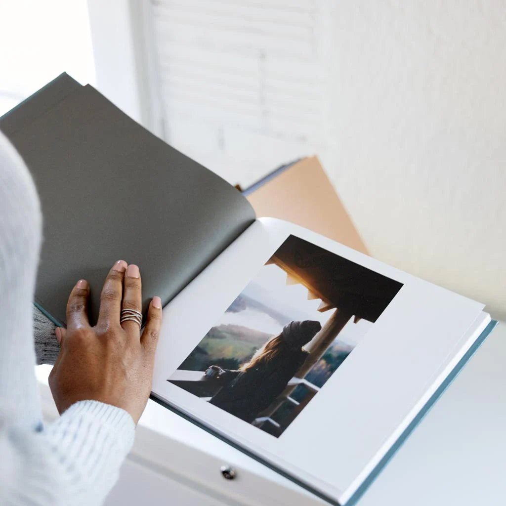 Person turning pages of a hardcover photo book showing a single landscape photograph printed on thick white paper.