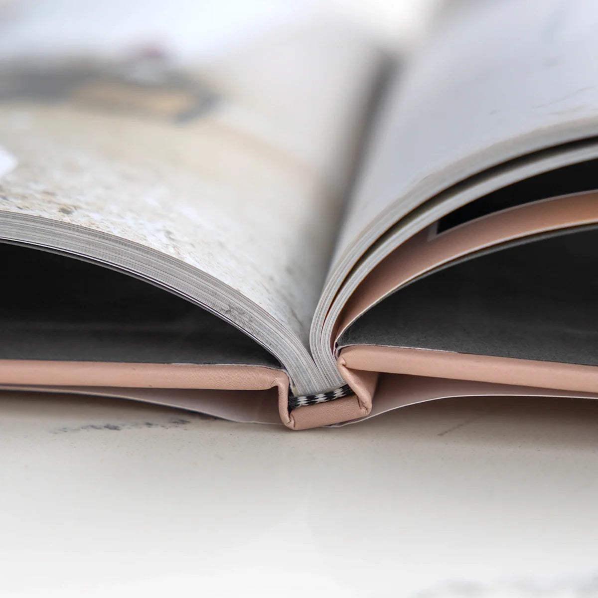 Close-up of an open hardcover photo book showing curved page edges, stitched binding, and thick premium paper stock.