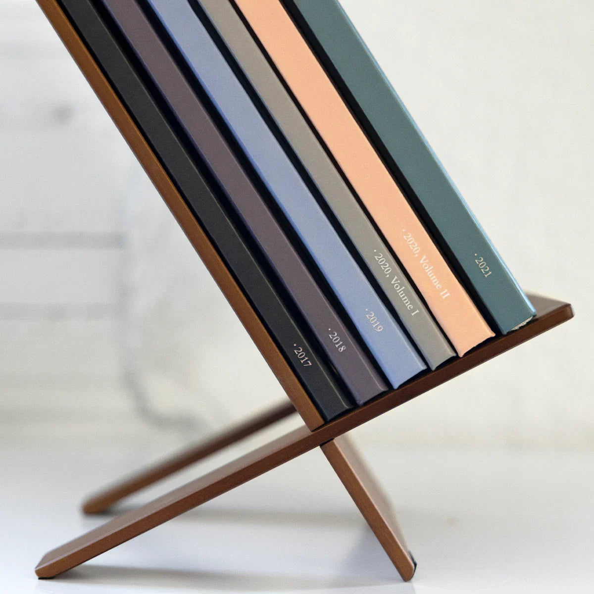 Set of hardcover photo books in assorted muted colors arranged upright on a wooden display stand with year and volume text on spines.