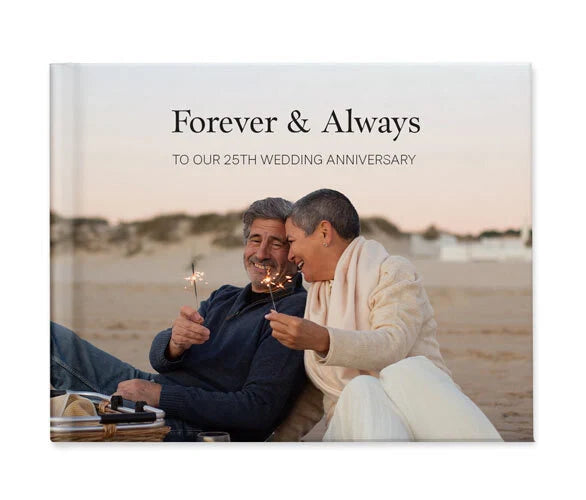 Hardcover photo book cover featuring a couple sitting on beach holding sparklers, with anniversary title text and warm sunset background.