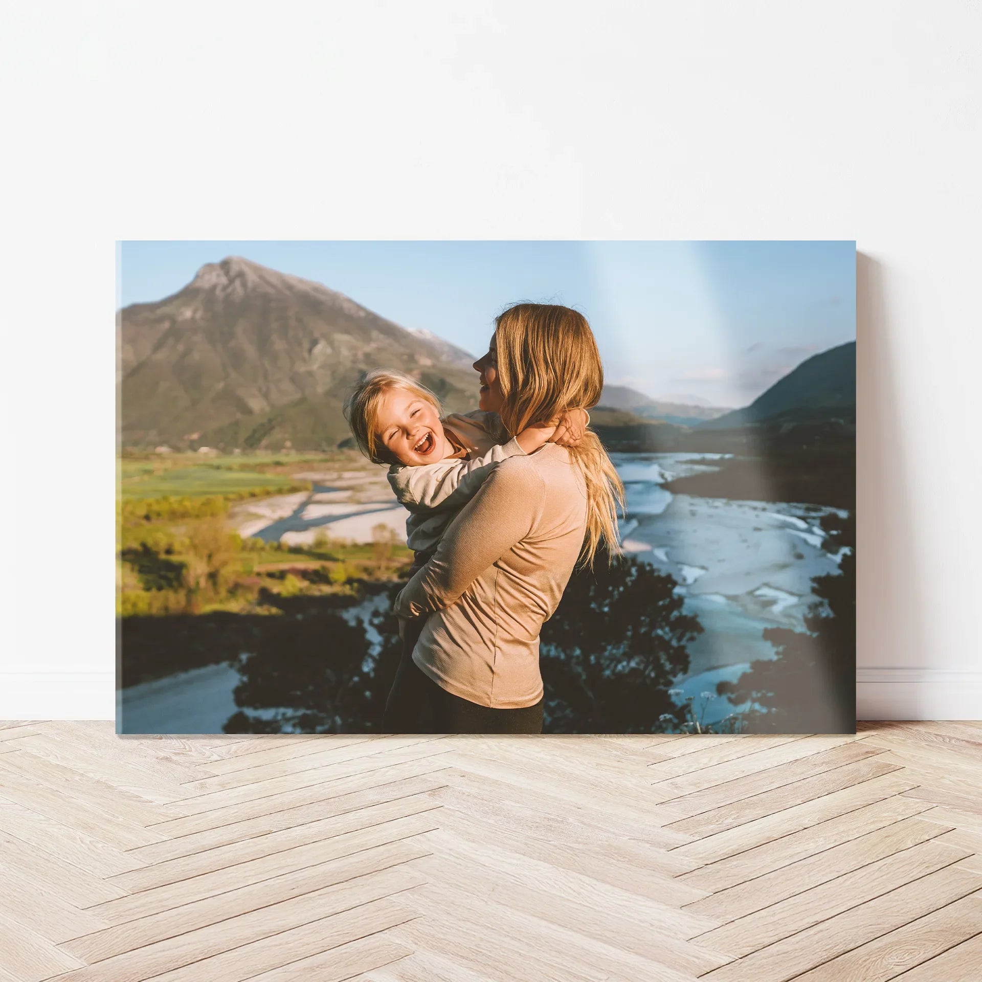 Acrylic wall print showing a person holding a child while overlooking a river valley with mountains and greenery in the background.