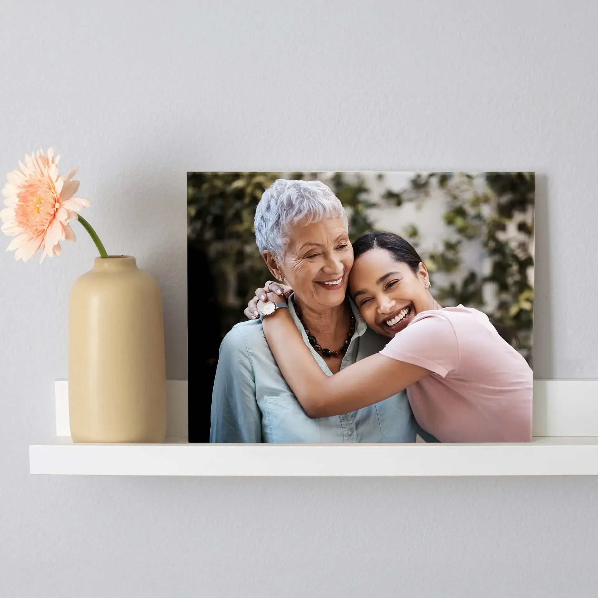 Acrylic wall print featuring two people smiling and embracing, displayed on a white shelf next to a beige vase with a single flower.