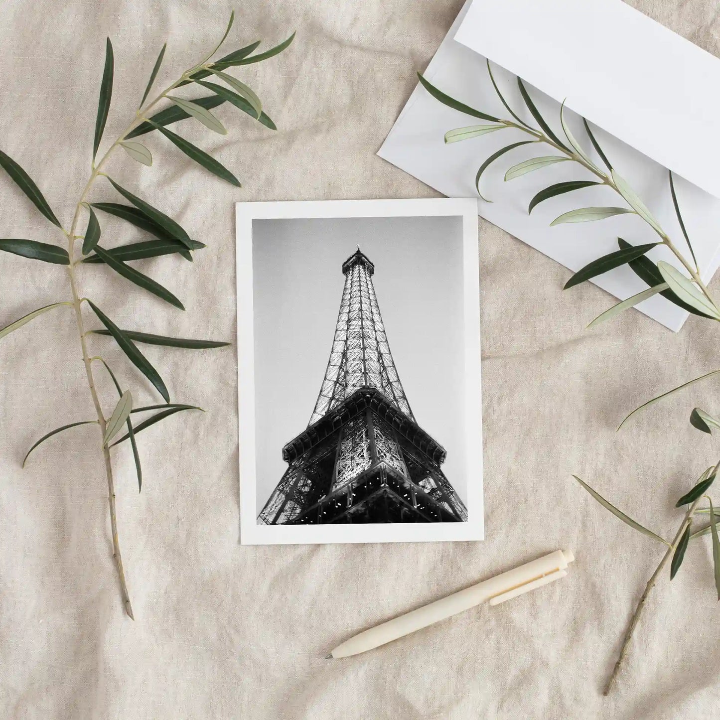 Flat card featuring a black-and-white Eiffel Tower image, styled on textured fabric with greenery, envelope, and pen nearby.