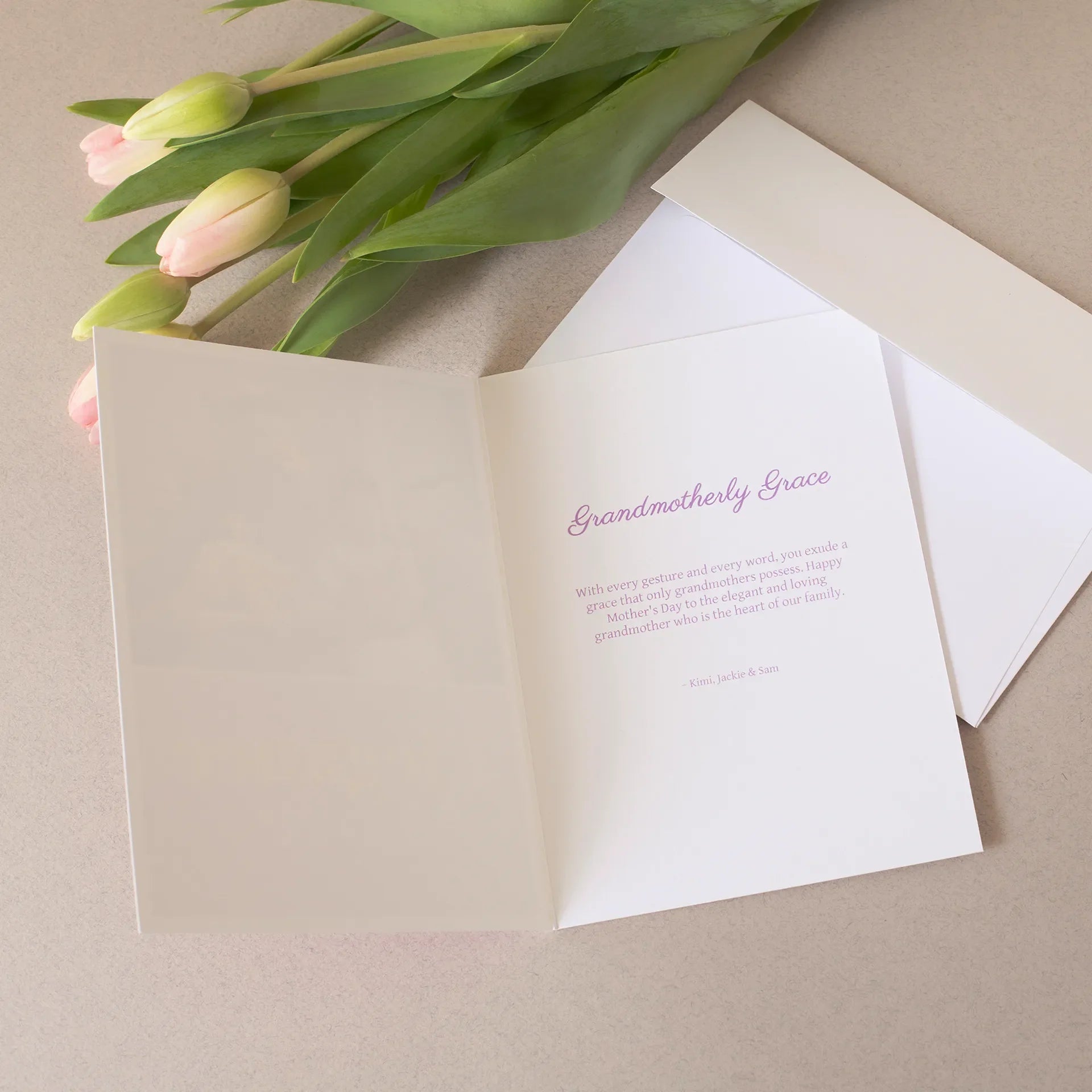 Open folded Mother’s Day card with pink “Grandmotherly Grace” message inside, displayed beside tulips and matching white envelope.