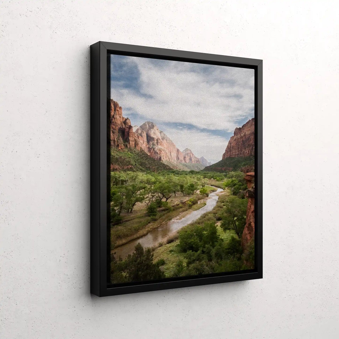 Black framed canvas print of a scenic canyon landscape with red rock cliffs and winding river, displayed on a textured white wall.