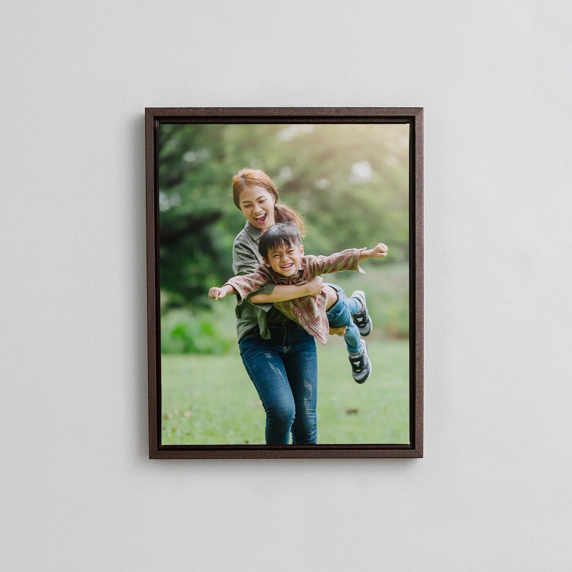 Dark wood framed canvas featuring a joyful mother lifting and spinning her young son in a green park setting.
