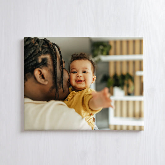 Canvas print featuring a close-up of an adult holding a baby indoors, with the baby reaching forward and a crib visible in the background.