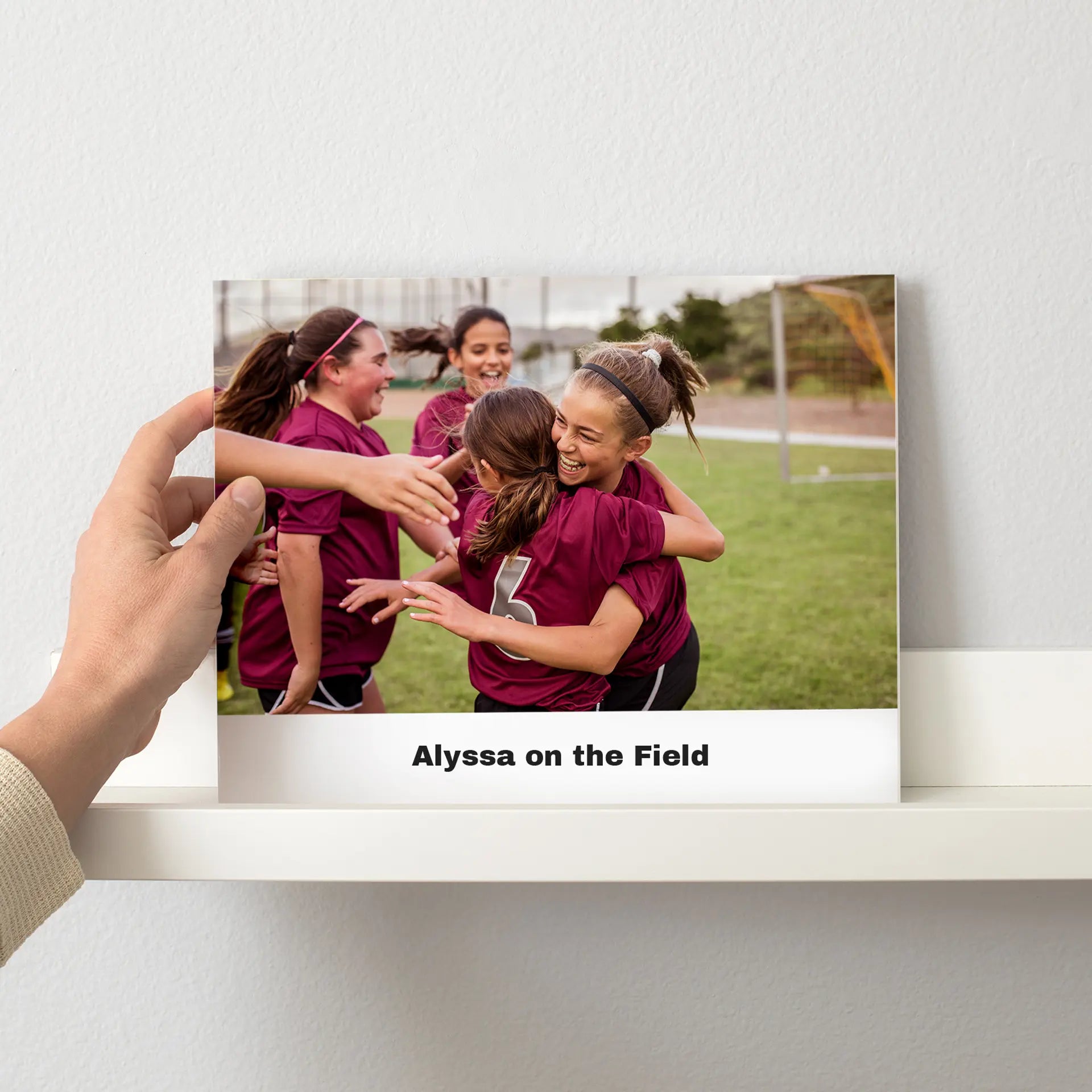 Printed photo displayed on a shelf showing a group of youth soccer players wearing matching jerseys and celebrating together on a field