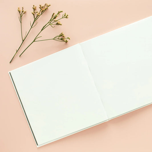 Open hardcover photo book on a pink background with a small branch of flowers
