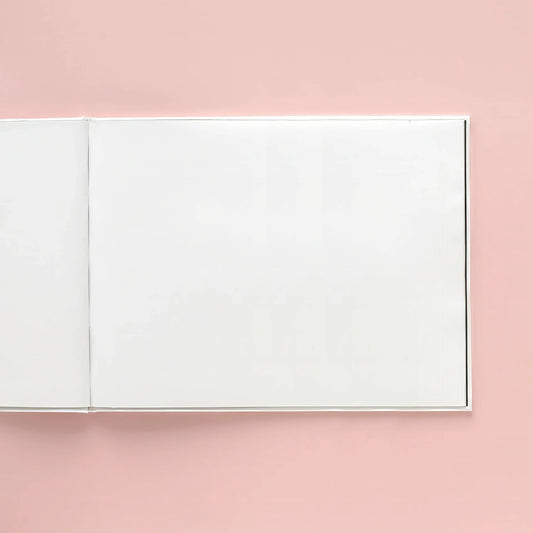 Open hardcover photo book with blank pages on a pink background