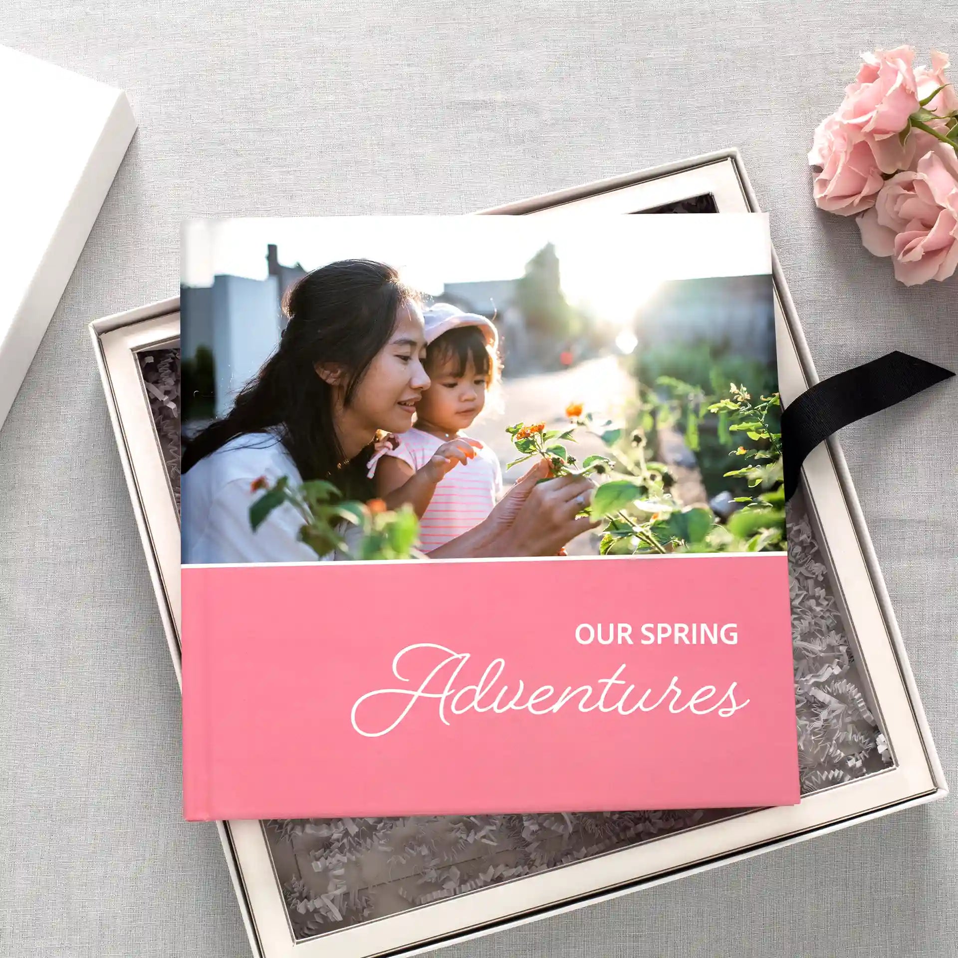 Layflat photo book with a pink cover titled “Our Spring Adventures,” featuring a mother and child on the cover, displayed inside a keepsake box.