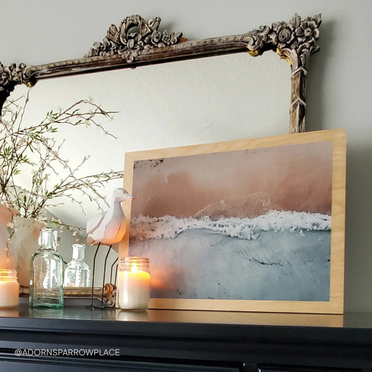 Maple wood print featuring an aerial view of waves meeting sand, displayed on a mantel with candles, glass bottles, and an ornate mirror.