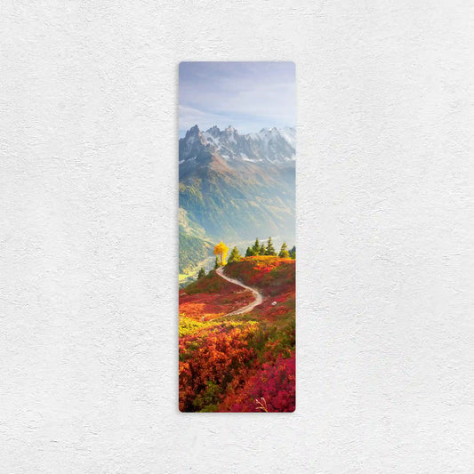 Vertical metal wall decor print of a winding path through bright red and green foliage leading toward a mountain range with snow-capped peaks.