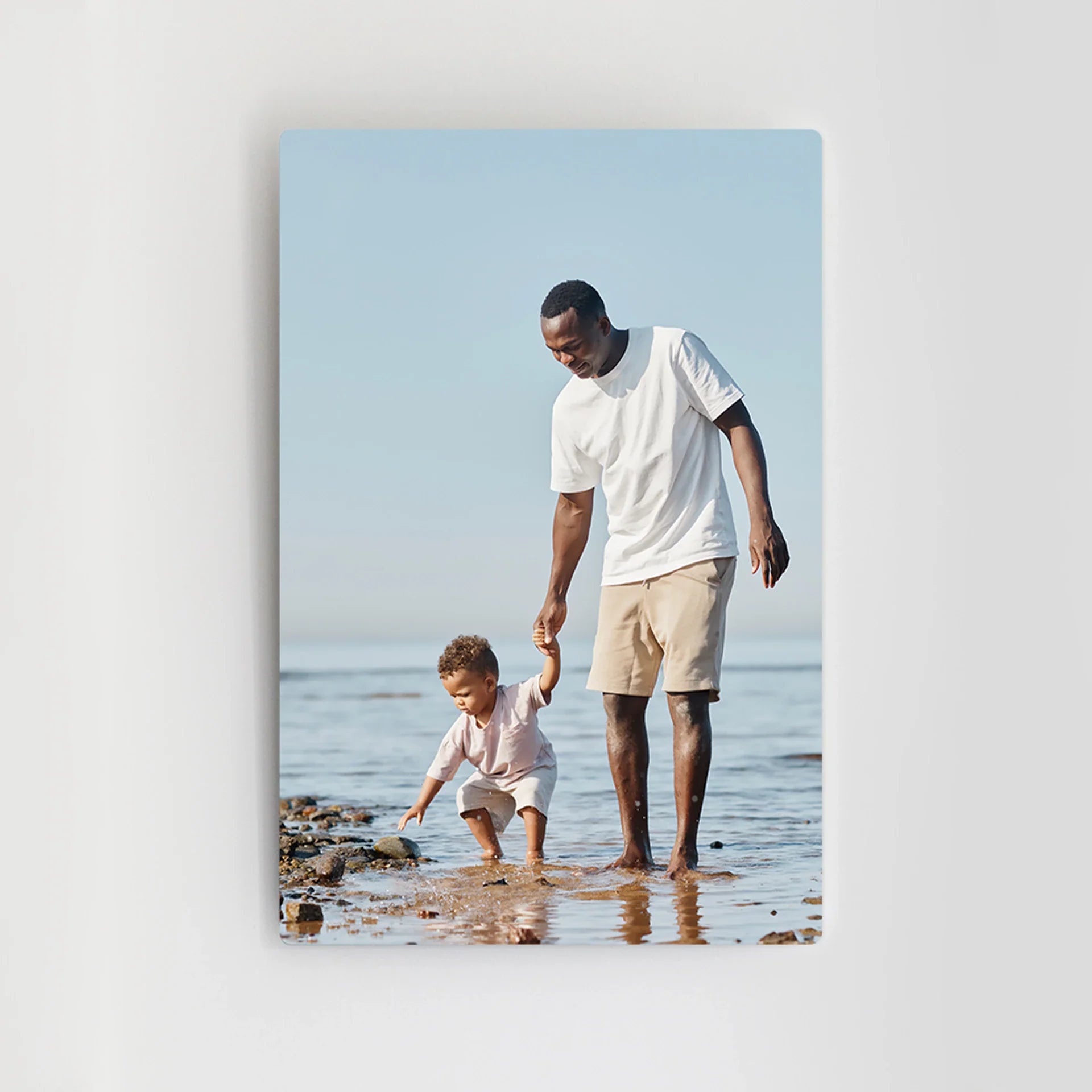 Metal wall print featuring a man holding a toddler’s hand while walking along a rocky shoreline, mounted vertically on a white wall.