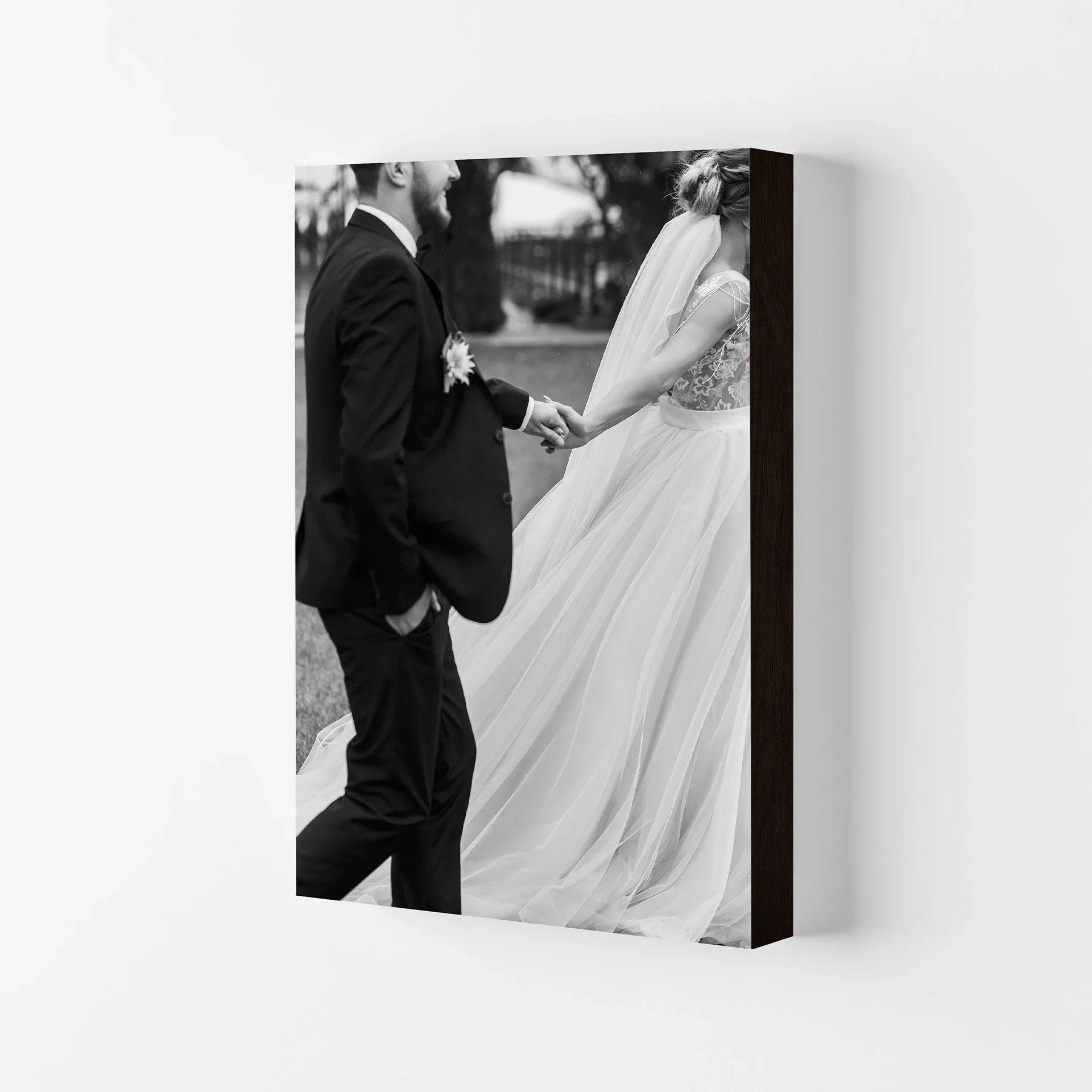 Mounted print with black-and-white wedding photo of a couple holding hands, thick block profile with dark edge, displayed on neutral wall.