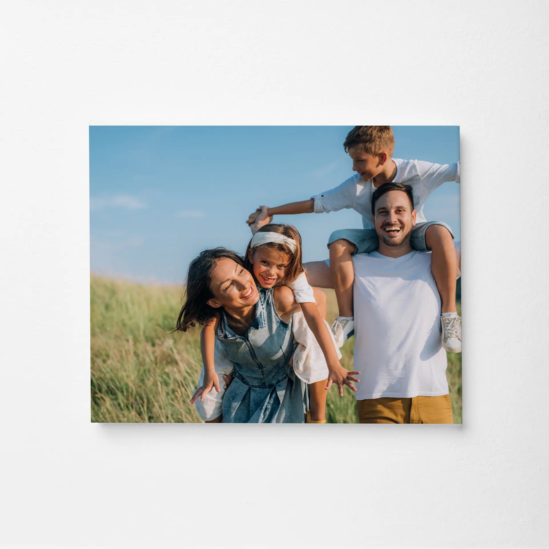 Mounted print showing smiling family with two children outdoors in grassy field, landscape orientation, clean edge profile, displayed on light wall.