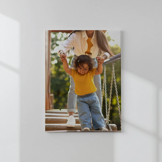 Mounted photo print of an adult holding a toddler’s hands while walking down playground steps, displayed on a white interior wall.