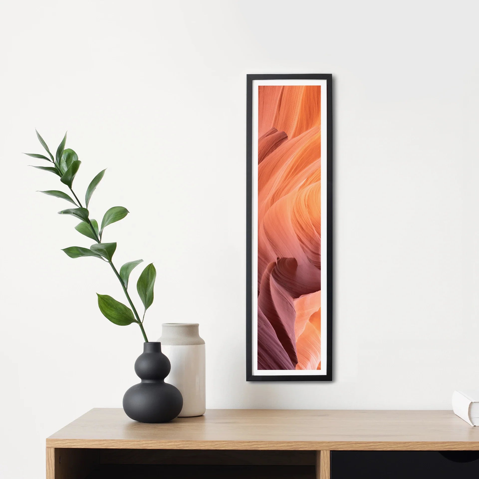 Tall narrow panoramic print in a black frame featuring layered sandstone textures, styled above a wooden console with decorative vases.