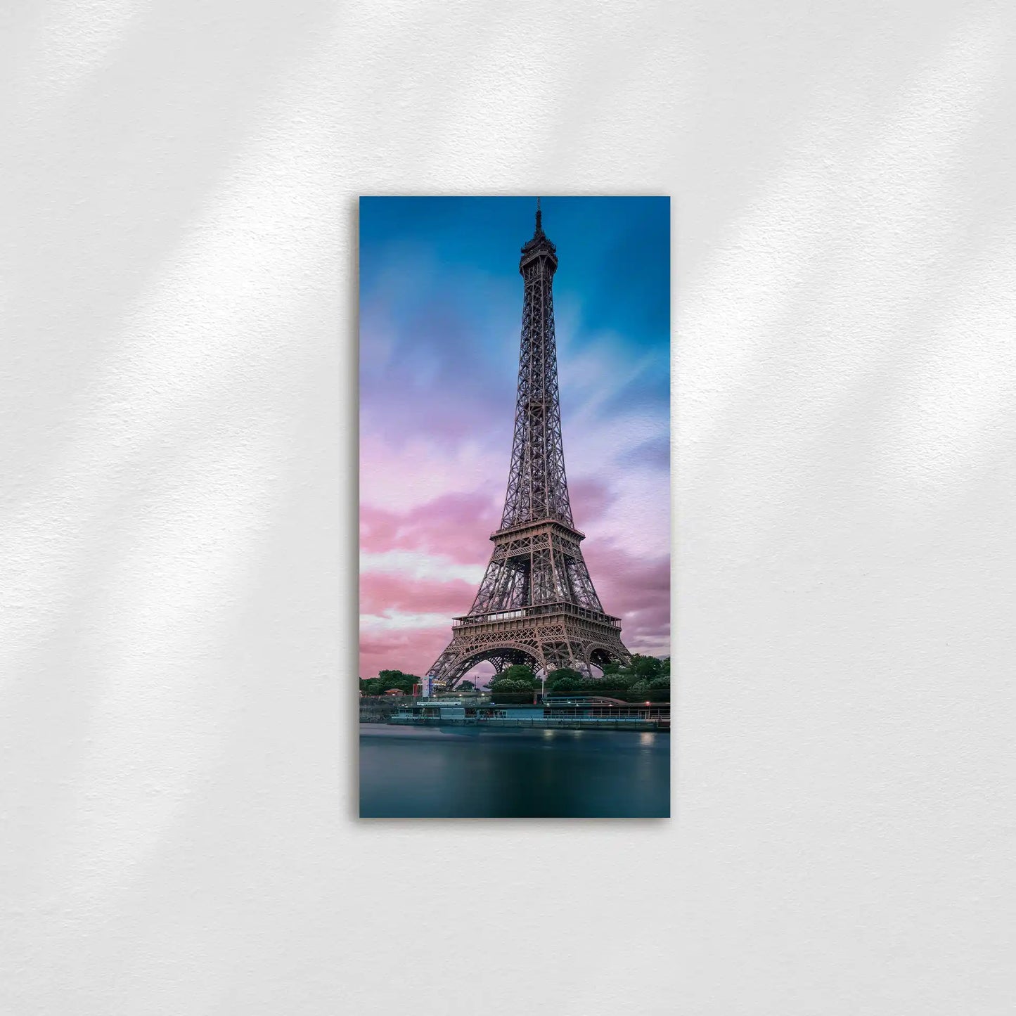 Panoramic wall print featuring the Eiffel Tower against a colorful sunset sky, mounted frameless on a light wall in a vertical layout.