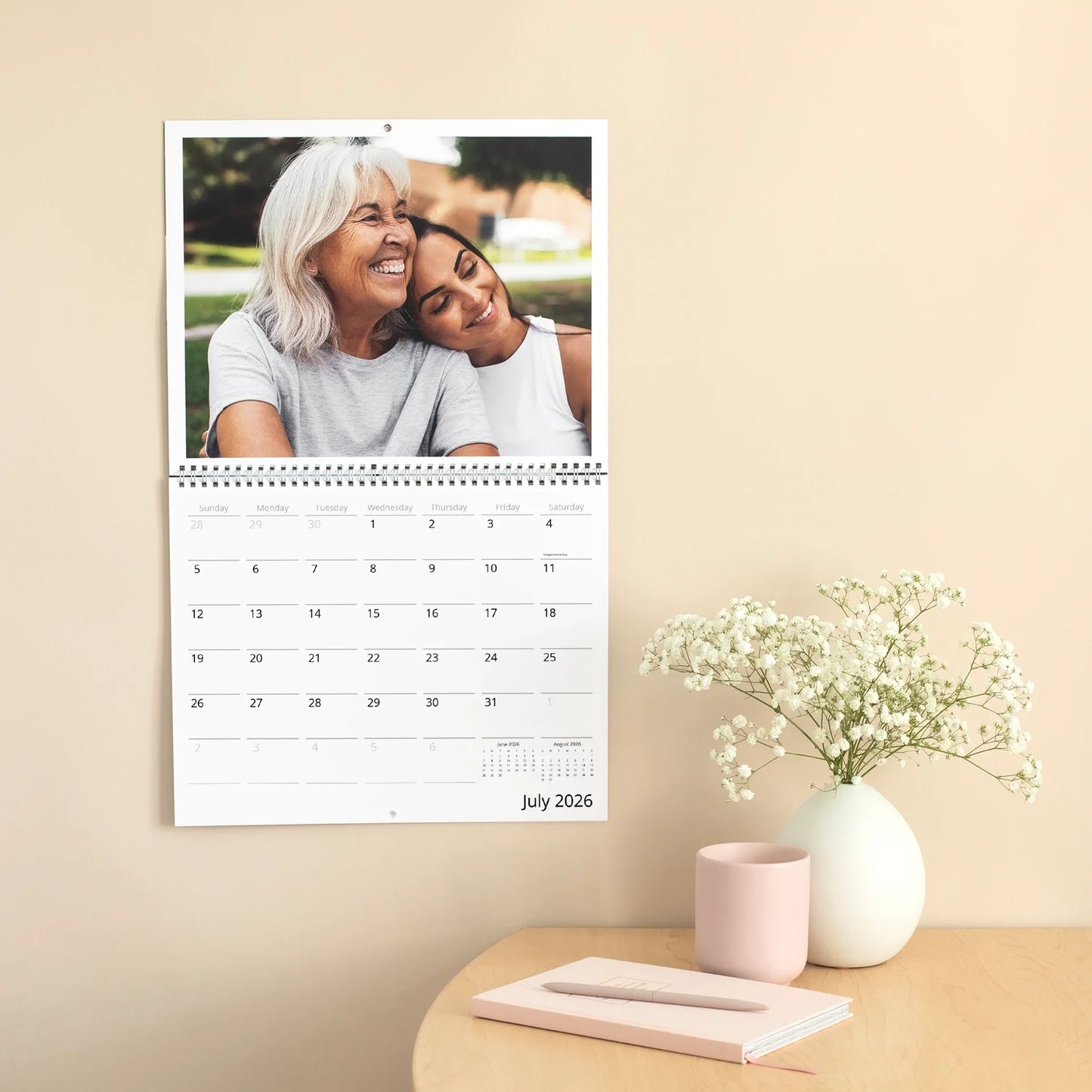 A wall calendar displaying a close-up portrait of an older woman and a younger woman smiling together, with a July 2026 grid below.