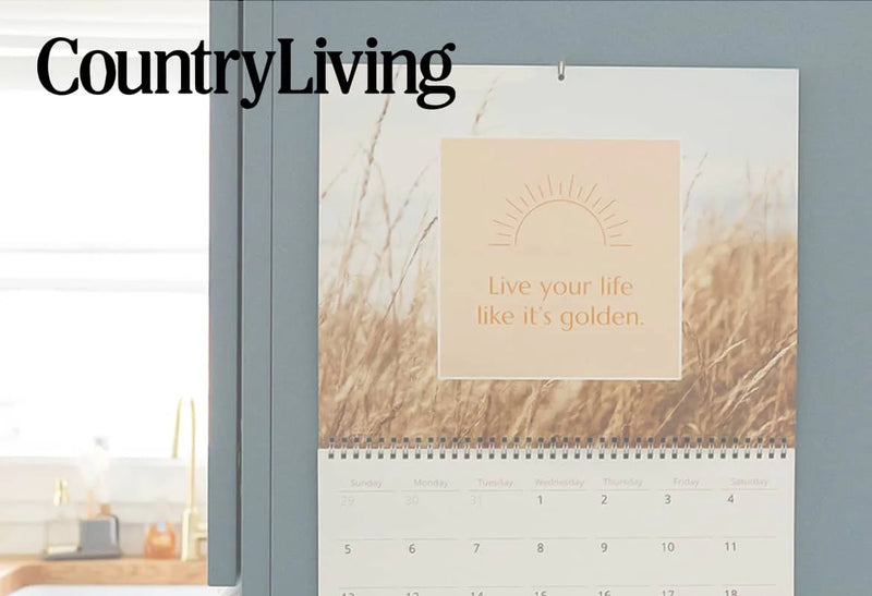 Wall calendar with a motivational quote “Live your life like it’s golden” hanging on a blue wall above a desk, with the Country Living logo.
