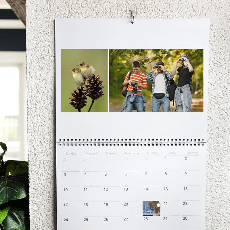 Wall calendar hanging outdoors with nature and photography images on top and a monthly date grid below.